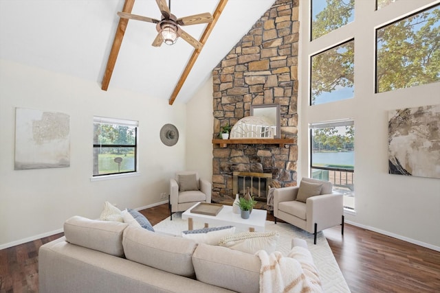 living area featuring beam ceiling, high vaulted ceiling, a stone fireplace, and wood finished floors