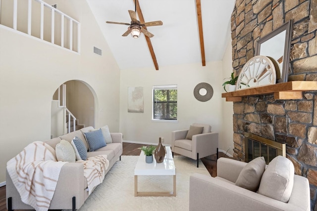 living area featuring wood finished floors, visible vents, high vaulted ceiling, arched walkways, and a stone fireplace