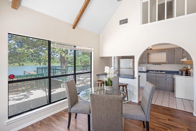 dining space with sink, a water view, high vaulted ceiling, dark hardwood / wood-style flooring, and beamed ceiling