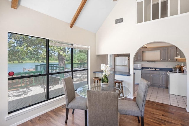 dining room with visible vents, a water view, beamed ceiling, wood finished floors, and high vaulted ceiling