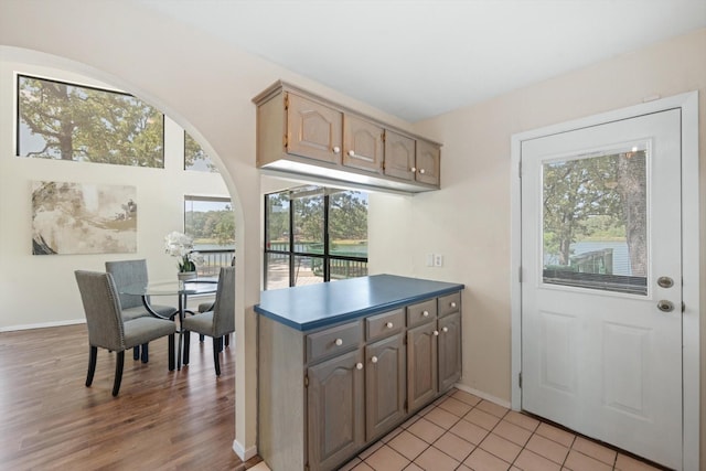 kitchen featuring light wood-style floors, a peninsula, dark countertops, and baseboards