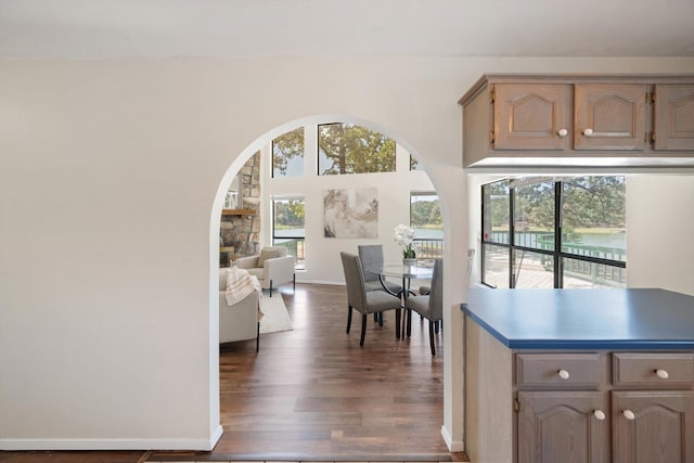 kitchen with baseboards, arched walkways, dark wood-type flooring, and a stone fireplace