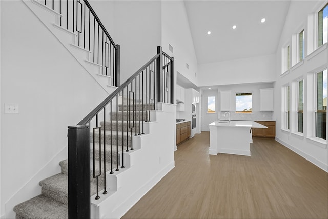 stairway with plenty of natural light, wood-type flooring, and high vaulted ceiling