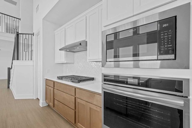 kitchen featuring backsplash, white cabinets, light hardwood / wood-style flooring, light brown cabinetry, and appliances with stainless steel finishes