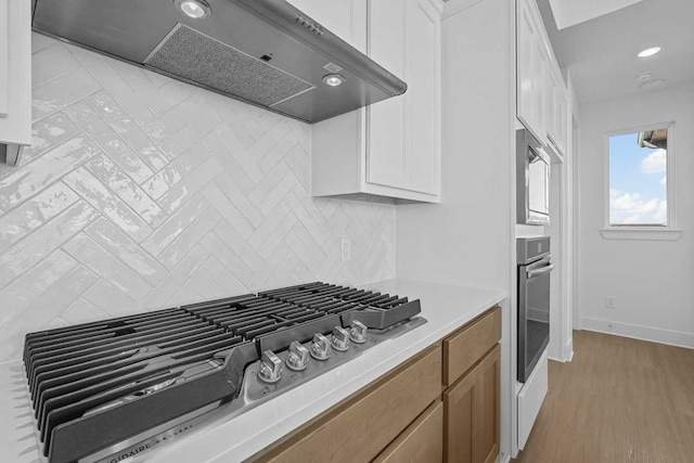 kitchen with light hardwood / wood-style flooring, white cabinets, stainless steel appliances, and ventilation hood