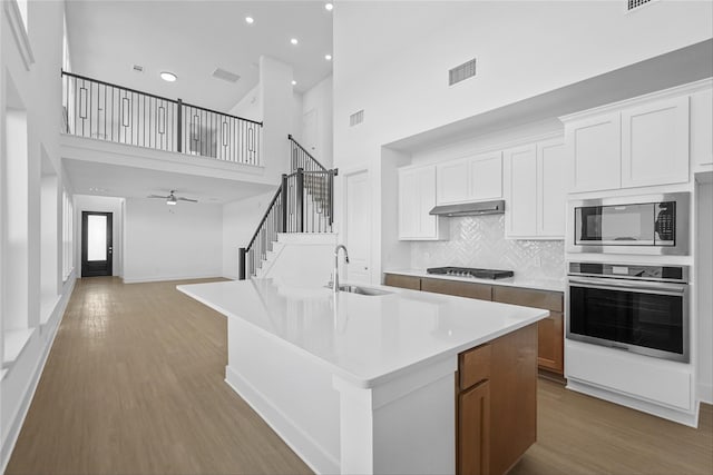 kitchen with a high ceiling, stainless steel appliances, white cabinetry, and a large island with sink