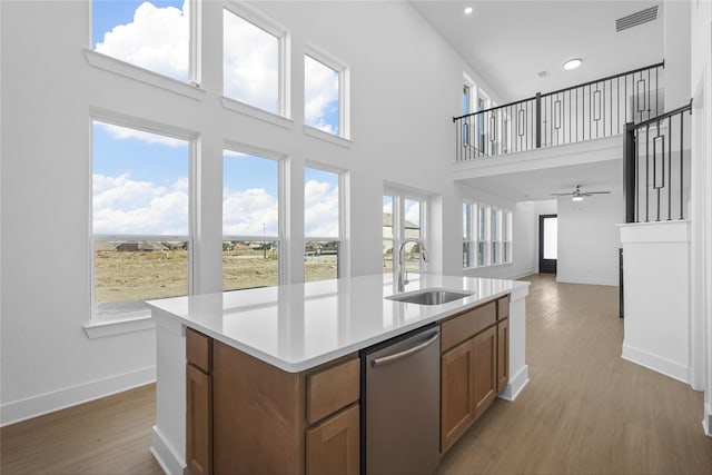 kitchen with dishwasher, a towering ceiling, a kitchen island with sink, and sink