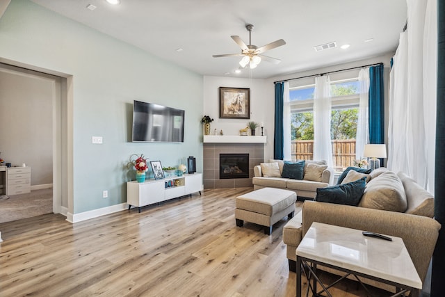 living room with a fireplace, light wood-type flooring, and ceiling fan