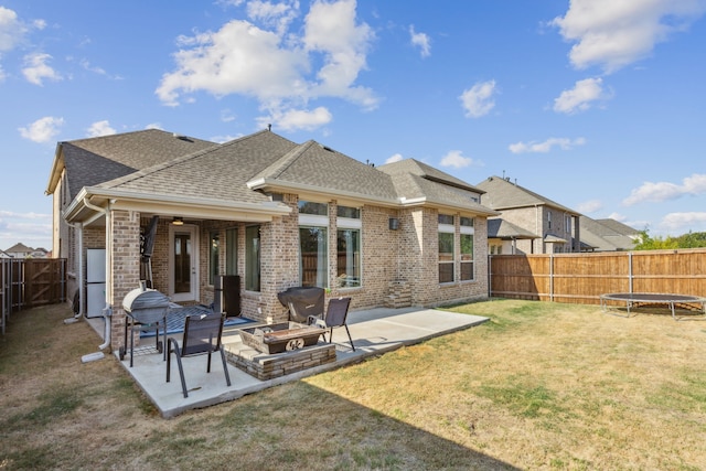 back of house with a fire pit, a yard, a patio, and a trampoline