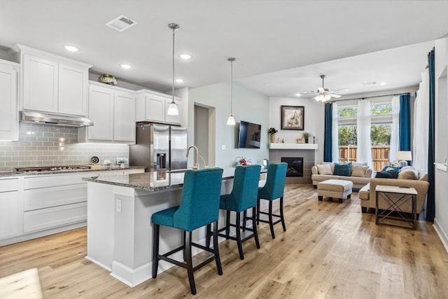 kitchen featuring dark stone counters, stainless steel appliances, ceiling fan, a breakfast bar, and a center island with sink