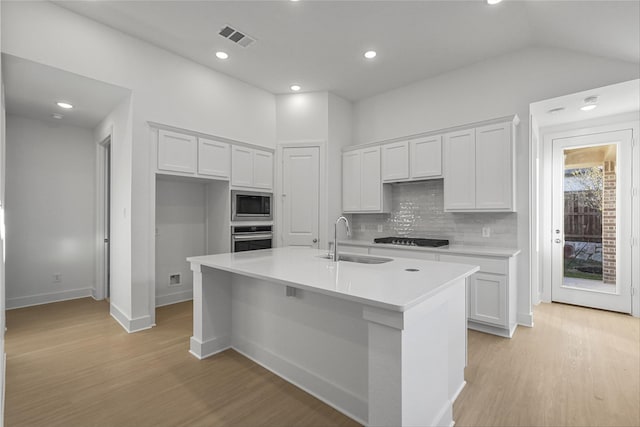 kitchen with appliances with stainless steel finishes, tasteful backsplash, sink, light hardwood / wood-style floors, and an island with sink