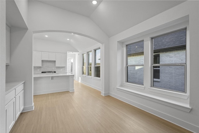 kitchen with white cabinets, light wood-type flooring, tasteful backsplash, and vaulted ceiling