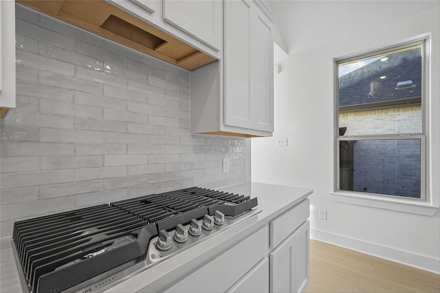 kitchen featuring white cabinets, decorative backsplash, light wood-type flooring, and stainless steel gas stovetop