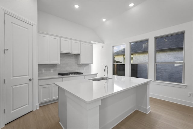 kitchen with sink, white cabinets, an island with sink, and vaulted ceiling