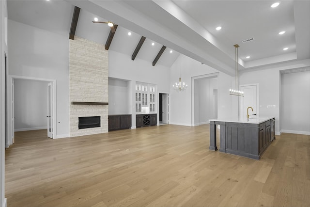 unfurnished living room with a fireplace, beamed ceiling, high vaulted ceiling, and light wood-type flooring