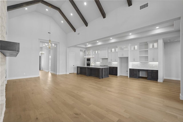 unfurnished living room featuring beam ceiling, light wood-type flooring, high vaulted ceiling, and an inviting chandelier