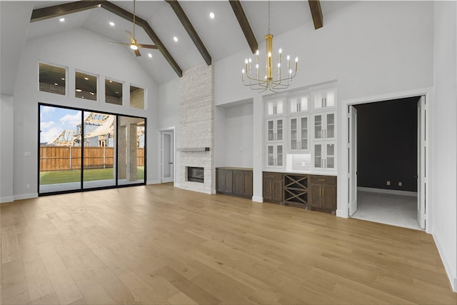 unfurnished living room with beam ceiling, a stone fireplace, high vaulted ceiling, and light hardwood / wood-style flooring