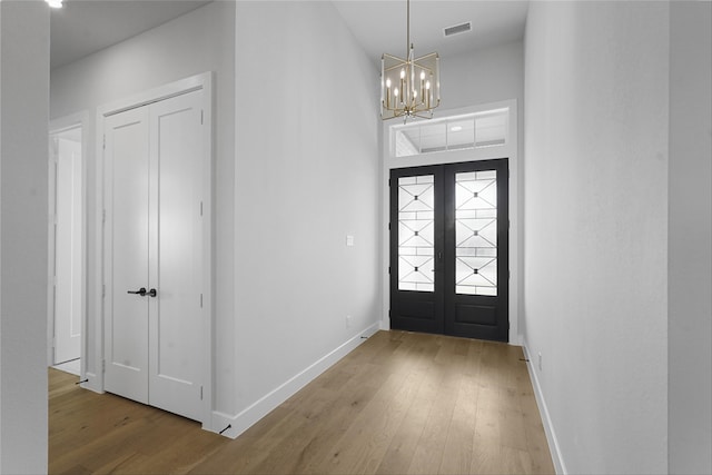 foyer with french doors, hardwood / wood-style floors, and an inviting chandelier