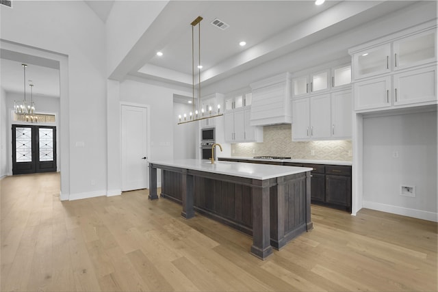 kitchen with french doors, appliances with stainless steel finishes, light hardwood / wood-style floors, white cabinetry, and an island with sink