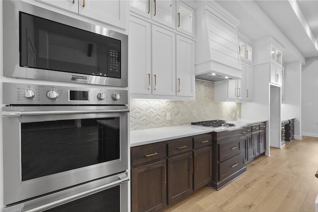 kitchen featuring backsplash, premium range hood, white cabinets, appliances with stainless steel finishes, and light hardwood / wood-style floors