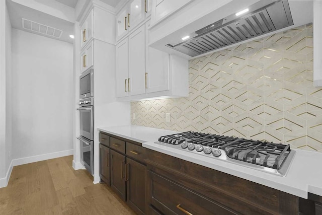 kitchen featuring white cabinets, custom range hood, appliances with stainless steel finishes, and tasteful backsplash