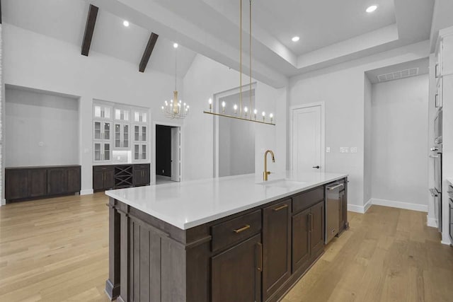 kitchen featuring a center island with sink, sink, light hardwood / wood-style flooring, beamed ceiling, and decorative light fixtures