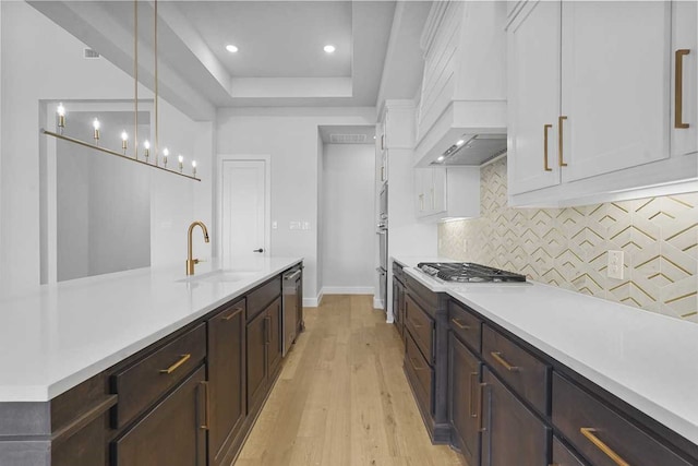 kitchen featuring white cabinetry, sink, pendant lighting, custom range hood, and light wood-type flooring