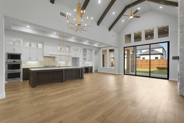 kitchen featuring stainless steel appliances, a kitchen island with sink, decorative light fixtures, high vaulted ceiling, and white cabinetry