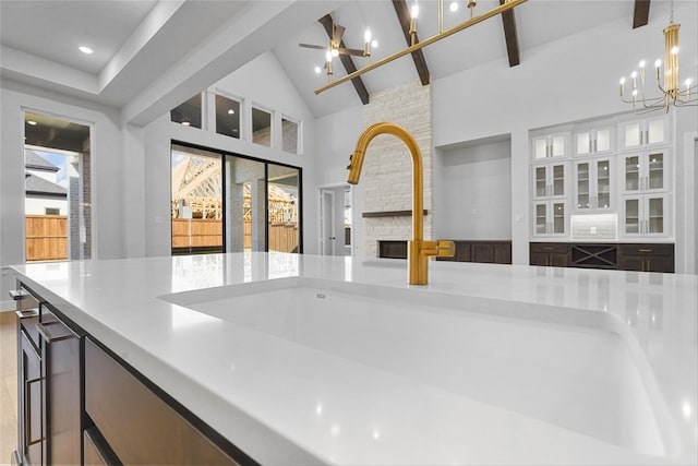 kitchen featuring sink, pendant lighting, high vaulted ceiling, beamed ceiling, and a stone fireplace