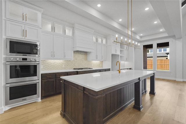 kitchen featuring a center island with sink, light hardwood / wood-style floors, appliances with stainless steel finishes, and pendant lighting