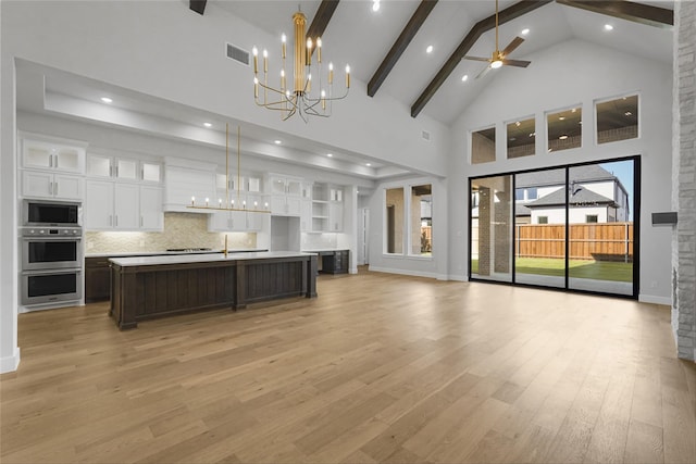 kitchen with pendant lighting, high vaulted ceiling, a center island with sink, appliances with stainless steel finishes, and white cabinetry