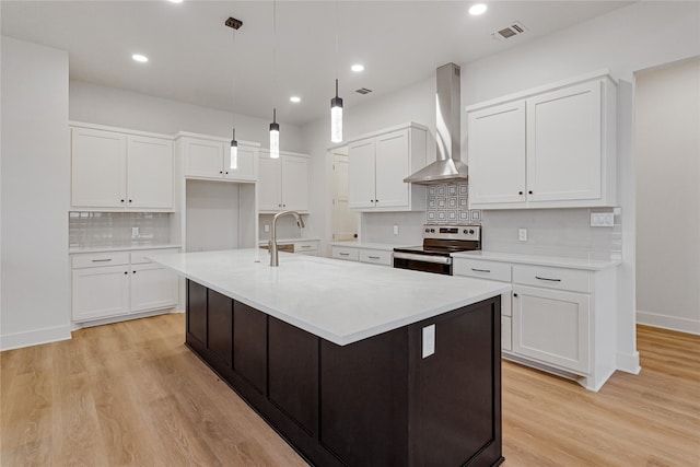 kitchen with visible vents, white cabinets, stainless steel range with electric cooktop, wall chimney range hood, and light wood-type flooring