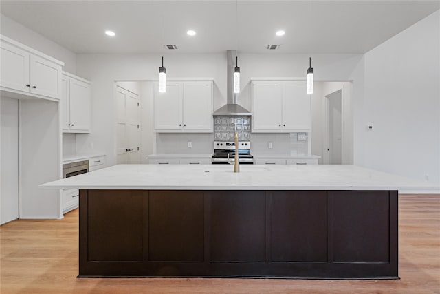 kitchen featuring light wood finished floors, white cabinets, electric stove, a large island, and wall chimney range hood