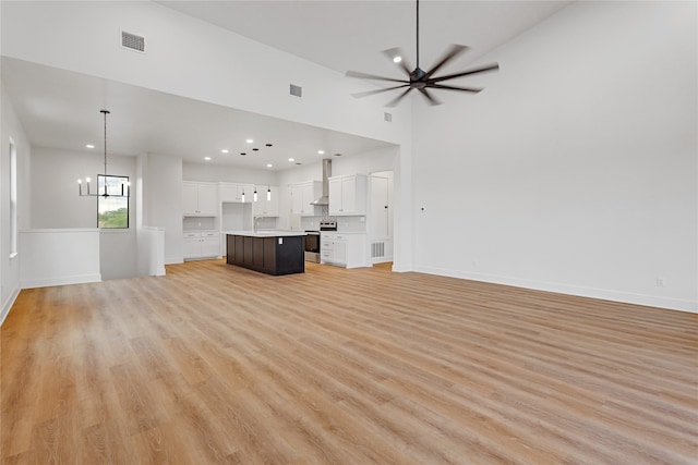 unfurnished living room featuring ceiling fan with notable chandelier, baseboards, visible vents, and light wood-style floors