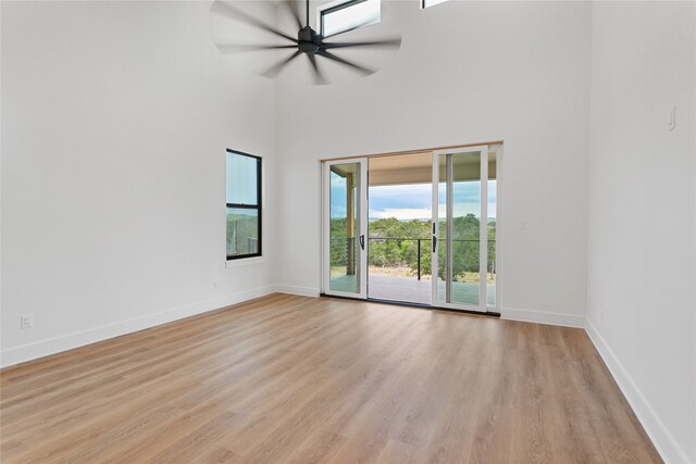 empty room featuring light wood-style floors, ceiling fan, a towering ceiling, and baseboards