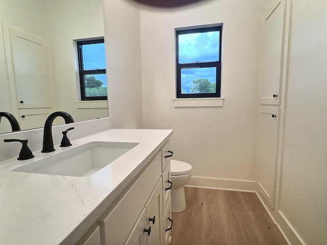 half bathroom with baseboards, vanity, toilet, and wood finished floors