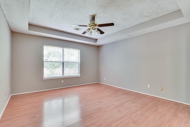 empty room featuring a raised ceiling, a textured ceiling, wood-type flooring, and ceiling fan