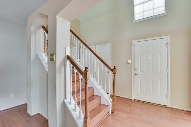 foyer entrance featuring a towering ceiling, a textured ceiling, and light hardwood / wood-style flooring