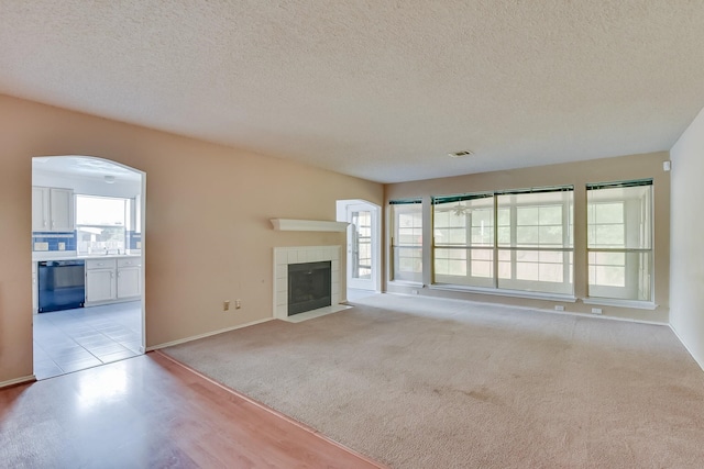 unfurnished living room featuring a textured ceiling, light colored carpet, and a tile fireplace