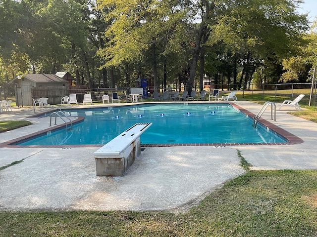 view of swimming pool featuring a diving board, a storage unit, and a patio area