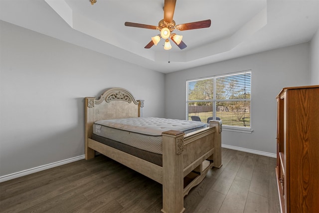 bedroom featuring a raised ceiling, dark hardwood / wood-style flooring, and ceiling fan