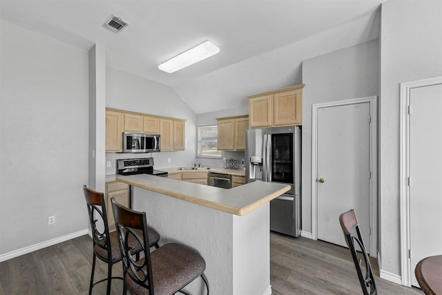 kitchen with light brown cabinets, lofted ceiling, hardwood / wood-style flooring, appliances with stainless steel finishes, and a breakfast bar