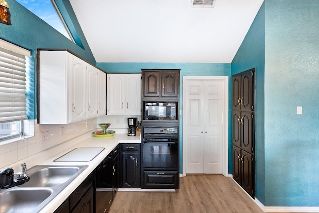 kitchen with vaulted ceiling, black appliances, decorative backsplash, white cabinets, and sink