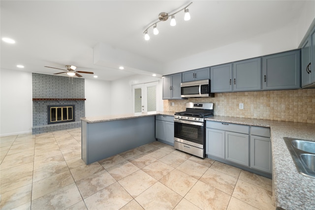 kitchen featuring backsplash, a brick fireplace, stainless steel appliances, kitchen peninsula, and ceiling fan