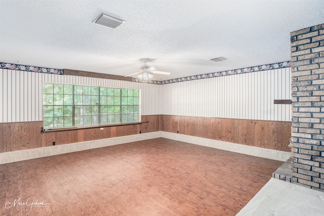 spare room with a textured ceiling, wood walls, and ceiling fan