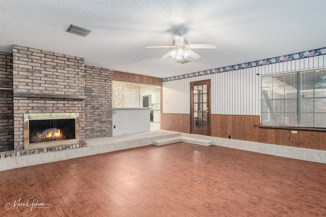 unfurnished living room with a textured ceiling, a brick fireplace, hardwood / wood-style flooring, ceiling fan, and wooden walls