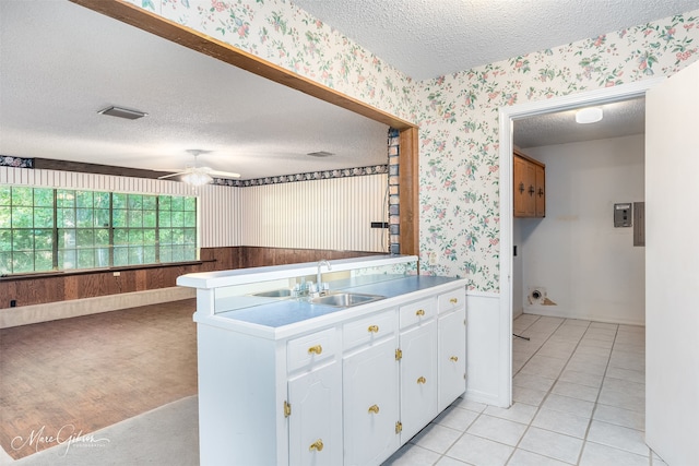 kitchen with white cabinets, wooden walls, sink, ceiling fan, and a textured ceiling