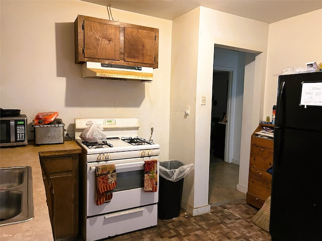 kitchen featuring white range with gas stovetop, under cabinet range hood, light countertops, freestanding refrigerator, and stainless steel microwave