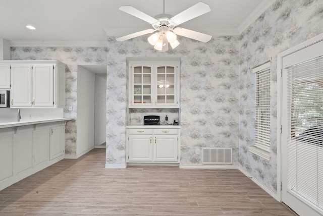 kitchen featuring visible vents, white cabinetry, crown molding, wallpapered walls, and baseboards
