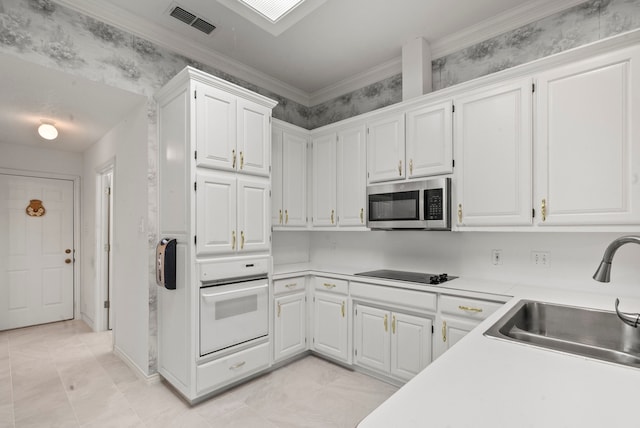 kitchen featuring black electric stovetop, oven, white cabinetry, and sink